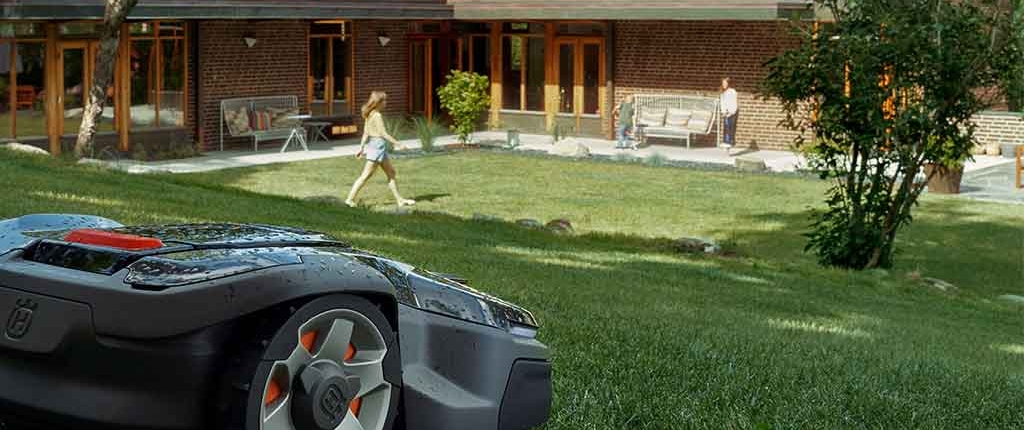 Husqvarna-Rasenroboter mäht die Wiese während Familie auf der Sonne spielt.