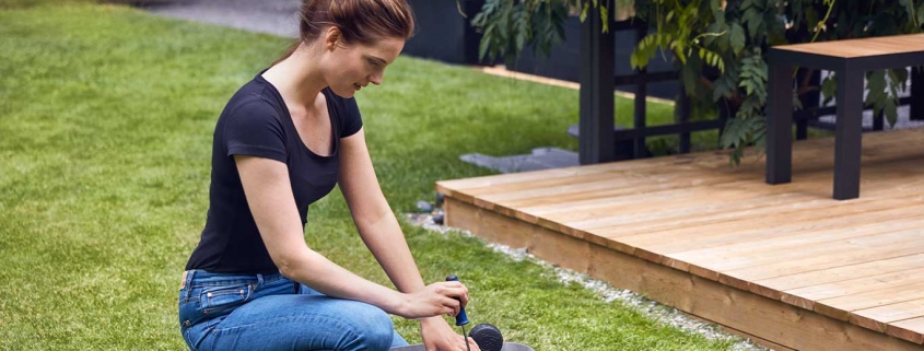 Frau arbeitet mit einem Akku-Rasenroboter nachhaltig im Garten.