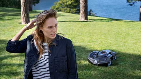 Frau im Garten beobachtet den Rasenmähroboter von Husqvarna