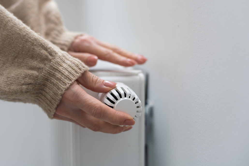 Frau dreht am Heizkörper-Thermostat.