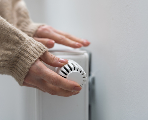 Frau dreht am Heizkörper-Thermostat.