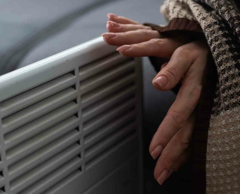 Frau wärmt sich die Hände an der Heizung.