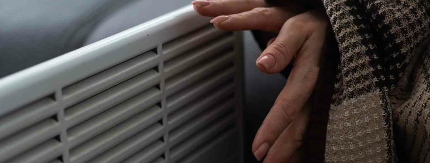 Frau wärmt sich die Hände an der Heizung.