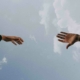 Zwei Hände, die versuchen, sich zu berühren vor bewölktem Himmel - Wir helfen Dir und nehmen Dich bei der Hand.